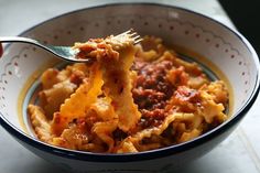 a bowl filled with pasta and meat on top of a table next to a fork