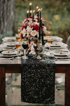 the table is set with black and white plates, silverware, candles, and flowers