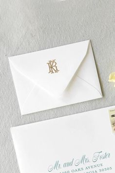 an envelope with a gold monogrammed initials on the front and bottom is sitting next to a yellow flower