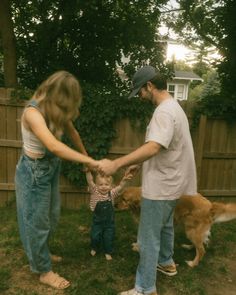 a man, woman and child holding hands with two dogs in the back yard near a fence