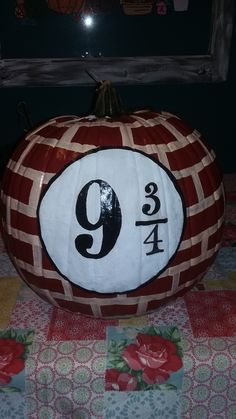 a red and white pumpkin with the number nine on it's side sitting on a quilted tablecloth