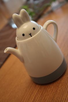 a white ceramic teapot with a rabbit face on it's side sitting on top of a wooden table