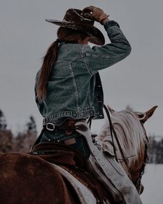 a woman riding on the back of a brown horse wearing a jean jacket and cowboy hat