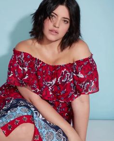 a woman sitting on the ground with her legs crossed and wearing a red floral dress