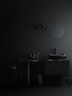 a black bathroom with two sinks and a round mirror above the sink is an empty chair