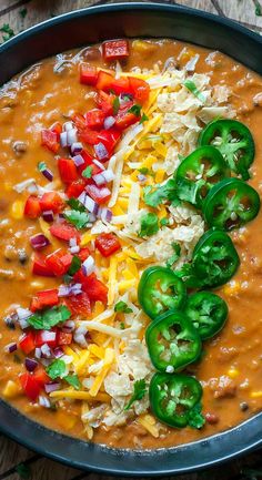 a bowl filled with beans, cheese and green peppers on top of a wooden table