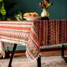 a colorful table cloth with tassels sits on a metal stand in front of a potted plant