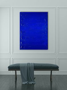 a blue painting hangs on the wall above a bench in a room with white walls