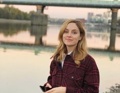 a woman standing in front of a body of water with a bridge in the background