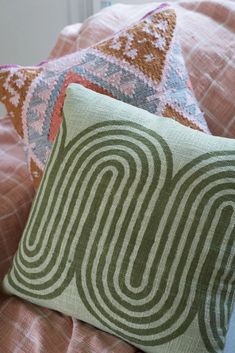 two pillows sitting on top of a bed covered in pink and green sheets with decorative designs