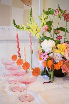 pink and yellow flowers are in vases on a table with wine goblets