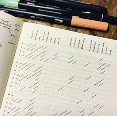 an open notebook sitting on top of a wooden table next to two pens and a calculator