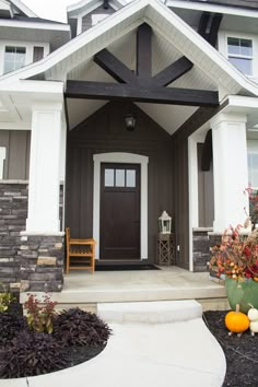 the front entrance to a house with two chairs and pumpkins in pots on the steps