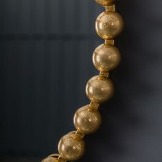 a gold beaded necklace hangs on a wall in front of a black background,