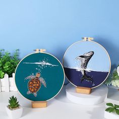 two cross stitch hoops with pictures of sea animals and turtles on them, sitting on a table