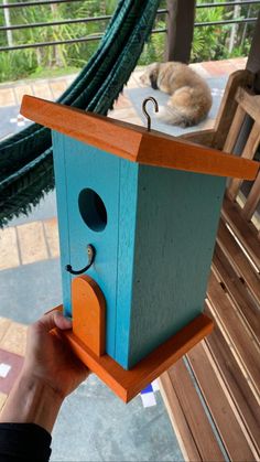 a person holding a bird house with a cat sleeping in the background