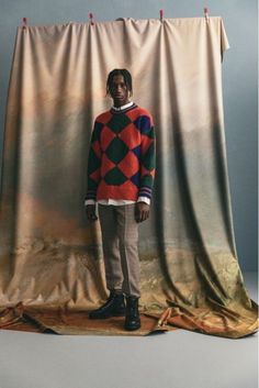 a man standing in front of a backdrop wearing a colorful sweater