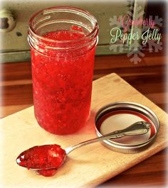 a jar filled with red liquid sitting on top of a wooden cutting board next to a spoon