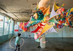 a man is playing with a dragon kite in an empty building while another person looks on