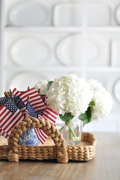 a basket with flowers in it and an american flag pinwheel on the side sitting on a table