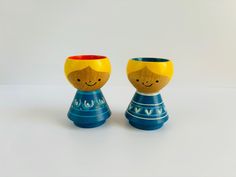 two small cups with faces painted on them sitting next to each other in front of a white background