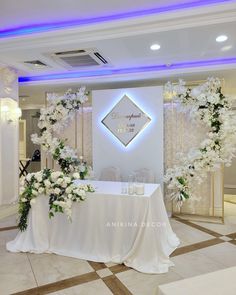 a table with white flowers and greenery on it in the middle of a room