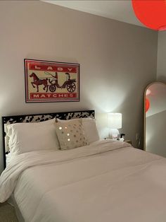 a bed with white sheets and pillows next to a red lamp on the side table