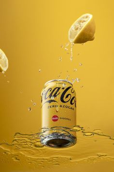 a can of coca - cola splashing into the water with two lemons on top