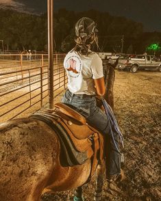 a woman riding on the back of a brown horse next to a wooden fence at night