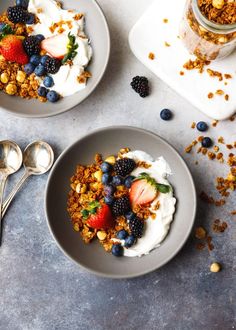 two bowls filled with granola, berries and yogurt on top of a table