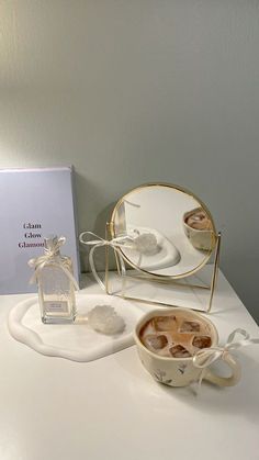 a white table topped with a cup of coffee next to a small mirror and box