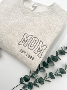 a t - shirt with the word mom printed on it sitting next to some flowers