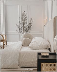 a bed with white linens and pillows in a bedroom next to a table with a vase on it