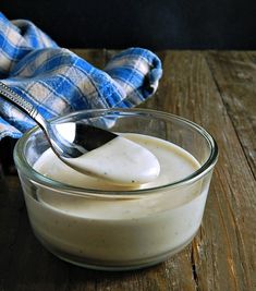 a glass bowl filled with yogurt sitting on top of a wooden table next to a blue and white towel