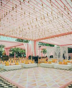 an outdoor wedding venue decorated with pink and yellow linens, gold pillows, and chandeliers