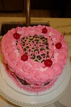 a heart shaped cake with pink frosting and cherries on top, sitting on a white plate