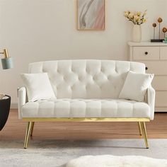 a white couch sitting on top of a hard wood floor next to a vase filled with flowers