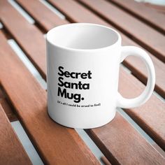 a white coffee mug sitting on top of a wooden bench with the words secret santa mug