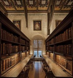 an old library filled with lots of books and wooden tables in front of paintings on the walls