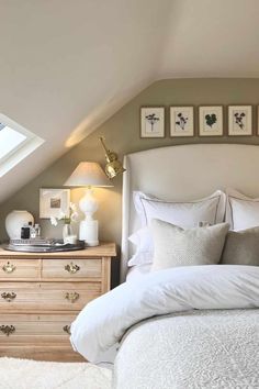 a white bed sitting under a window next to a wooden dresser and chest of drawers