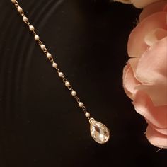 a close up of a necklace on a black surface with pink flowers in the background