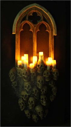 a bunch of candles that are sitting in front of a wall with skulls on it