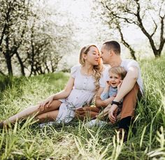 a man and woman are sitting in the grass with their son, who is kissing his nose