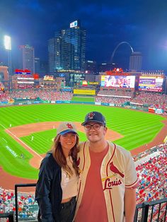 a man and woman standing in front of a baseball field