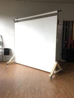 an empty room with a white board and ladder on the floor in front of it