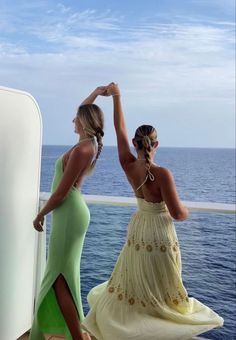 two women in dresses standing on the deck of a boat looking out at the ocean