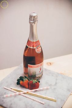 a bottle of wine and two strawberries on a marble tray with chopsticks