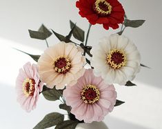 three flowers in a white vase with green leaves on the side and one red flower