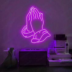 a purple neon sign with a praying hand in the center on a wall next to stacks of boxes