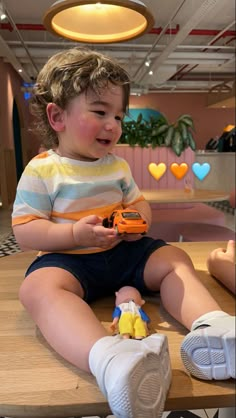 a little boy sitting on top of a wooden table holding a toy car in his hand